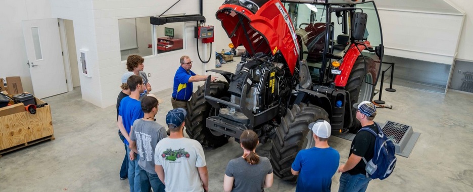 Instructor and a group of students look at a tractor.